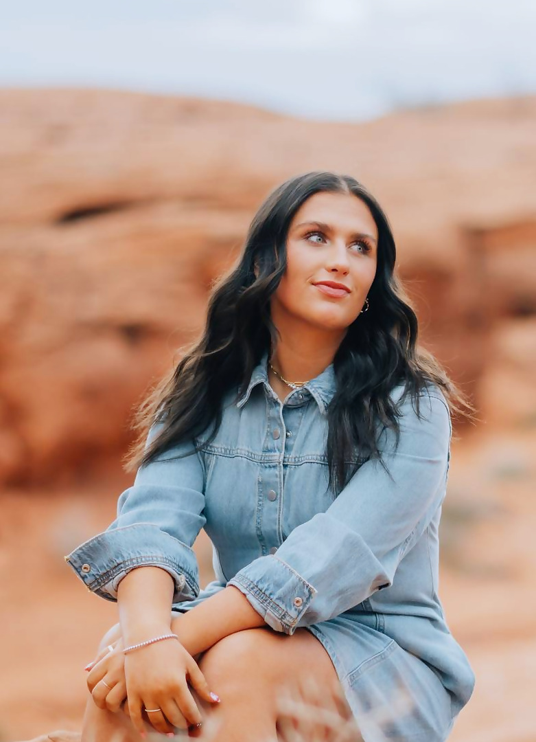 Kadence seated on a red sandstone ledge with her hands folded in her lap