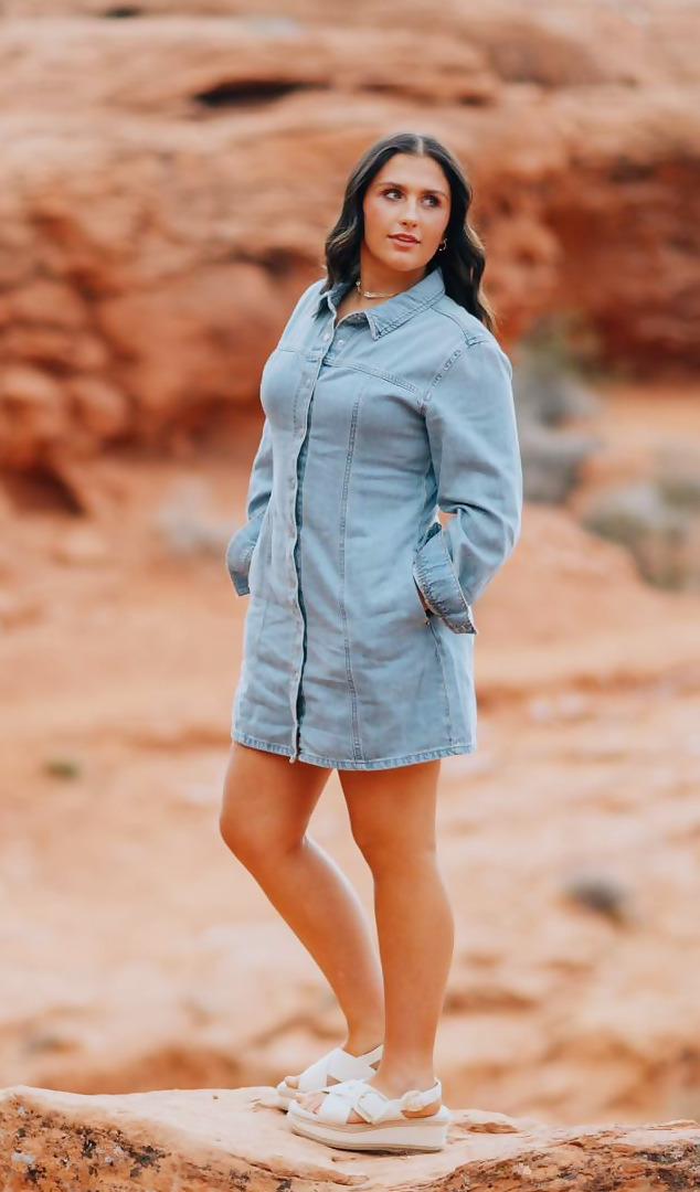 Kadence standing on a red sandstone outcrop in the desert wearing a denim dress