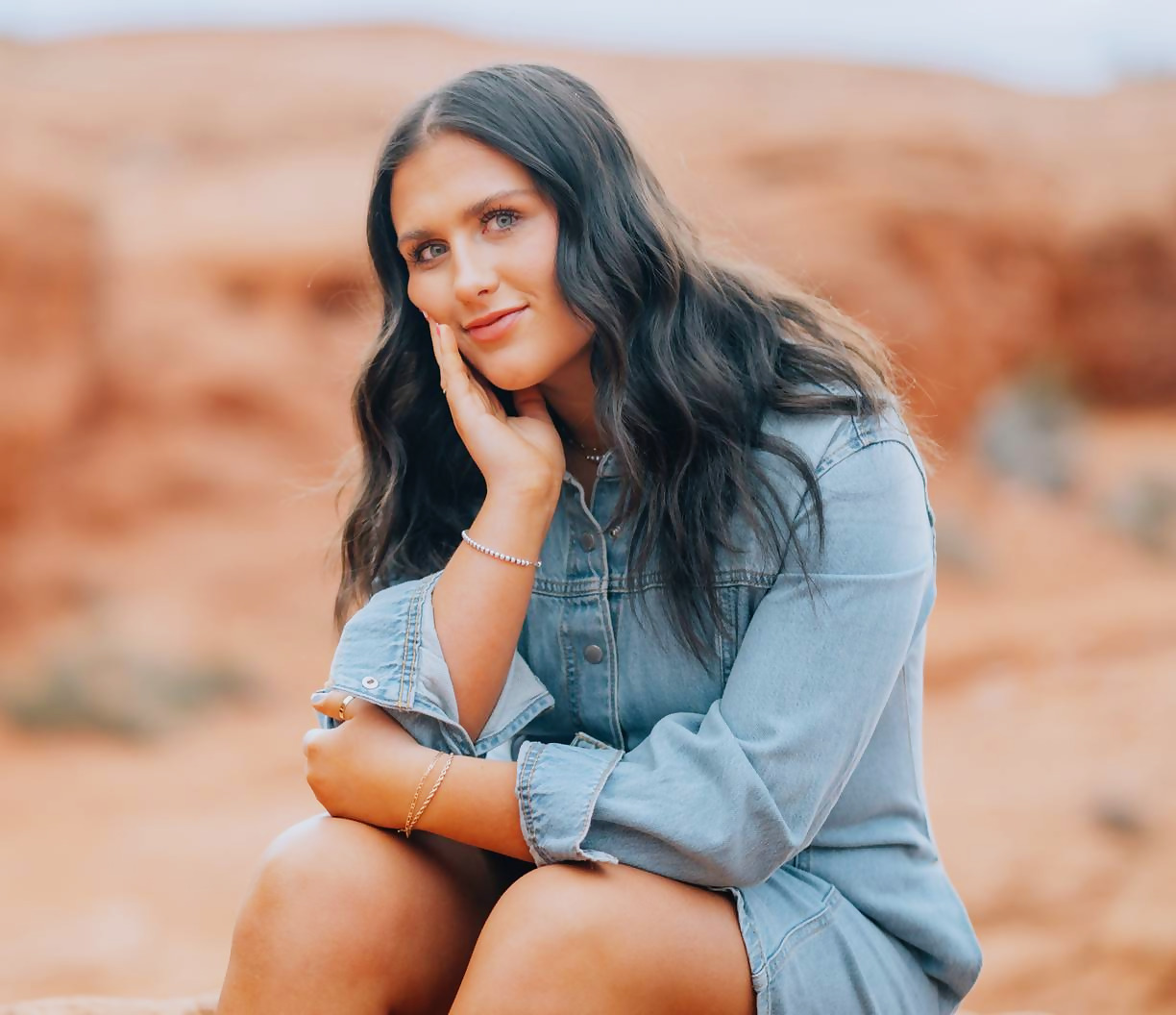 Kadence seated with her hand to her cheek against blurred red rock